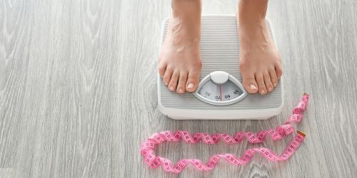 Image of a woman's feet on the weighing scales and a pink tape measure